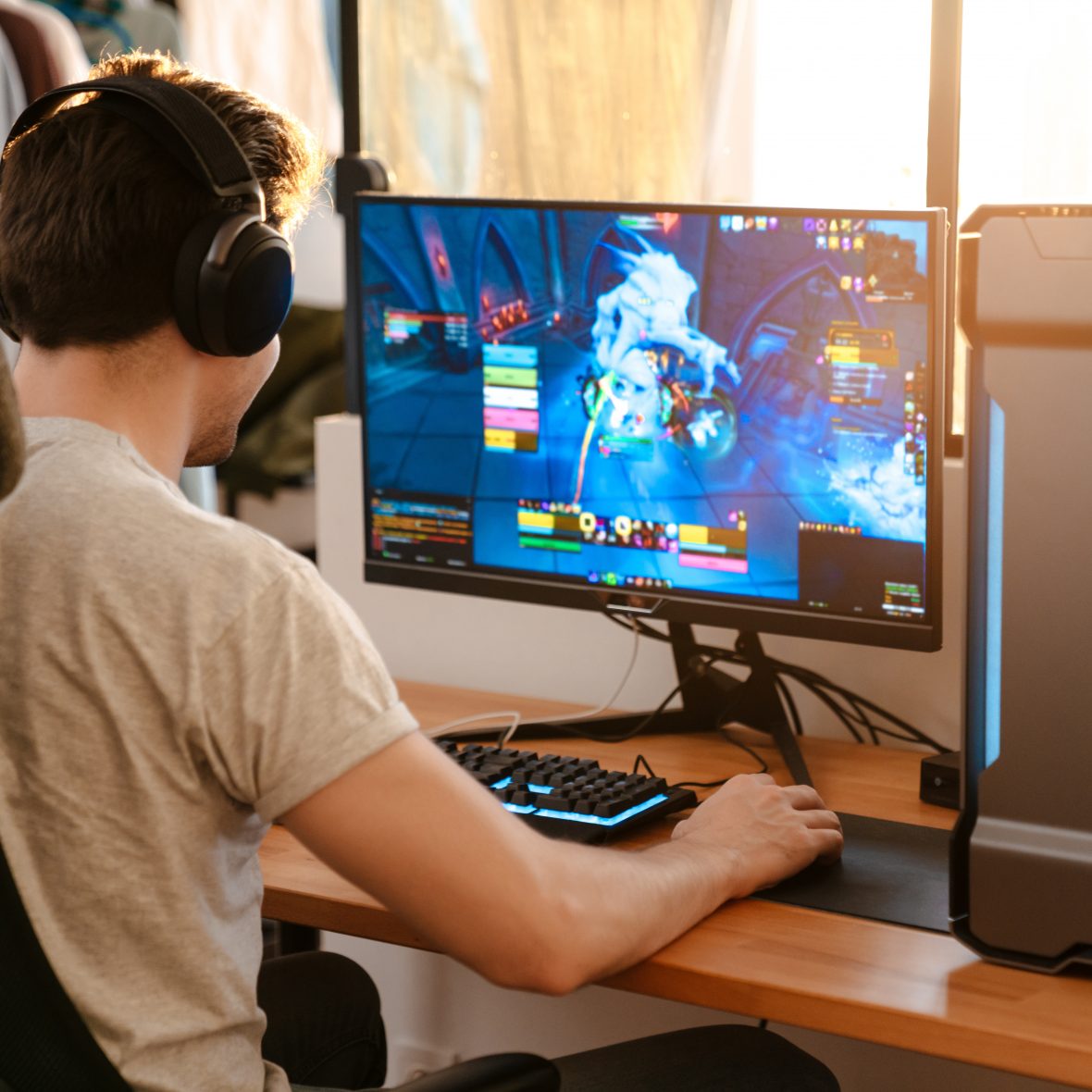 Caucasian brunette guy in headphones playing video game on his computer while sitting at home