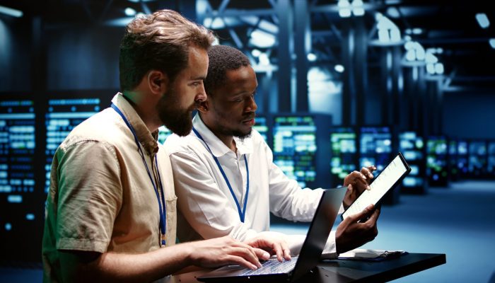 Coworkers running data center tests Coworkers running data center hardware diagnostic tests to determine and service software issues. Servicemen using laptop and tablet to fix critical systems, checking for blips